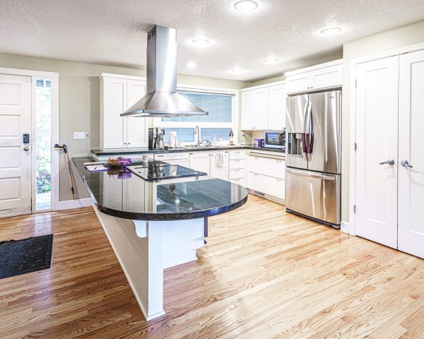 Kitchen pictured with roll-under peninsula counter and an overhead exhaust. The refrigerator and a set of double doors are in the background.